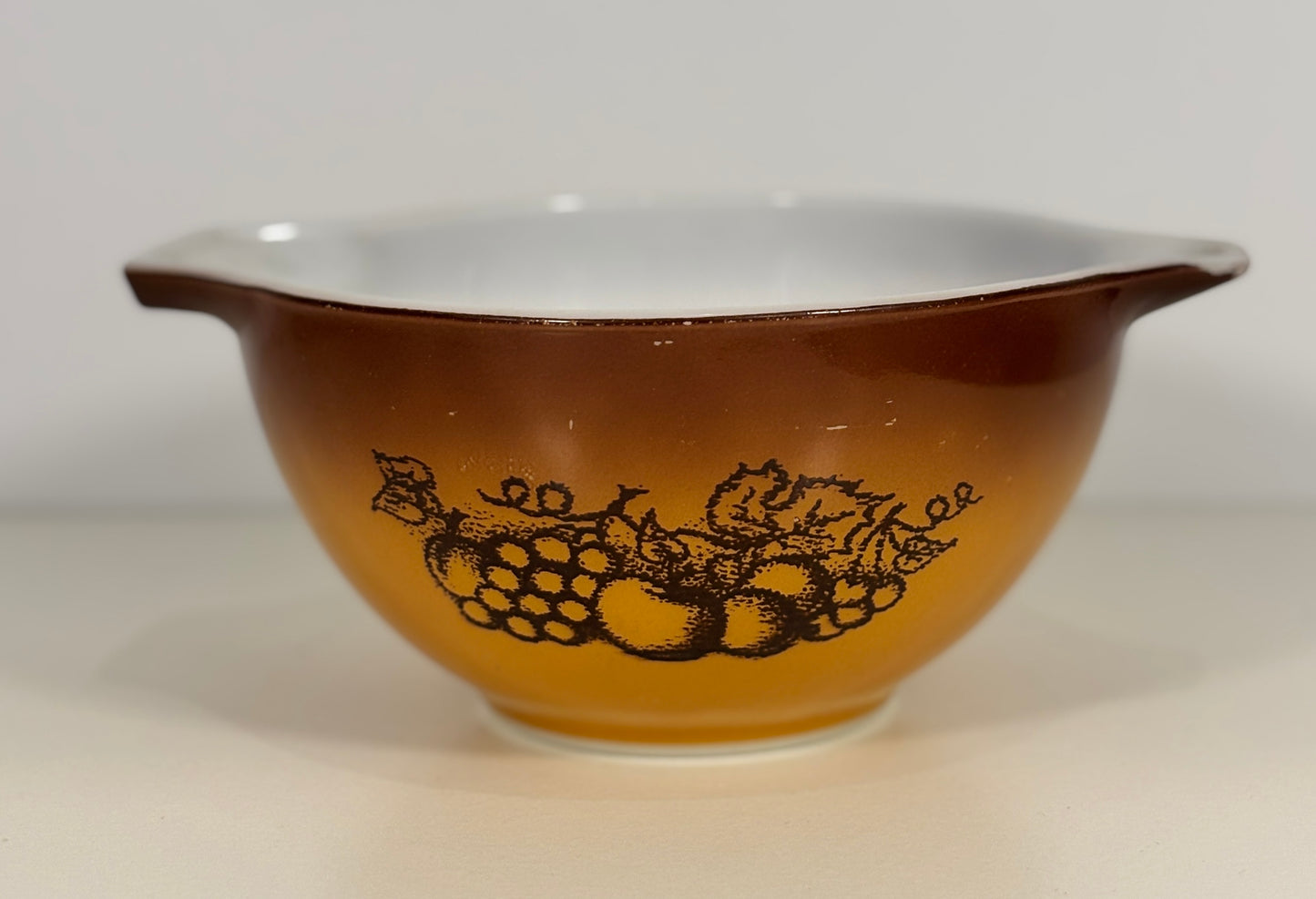 Brown Pyrex mixing bowl with fruit design on a white background