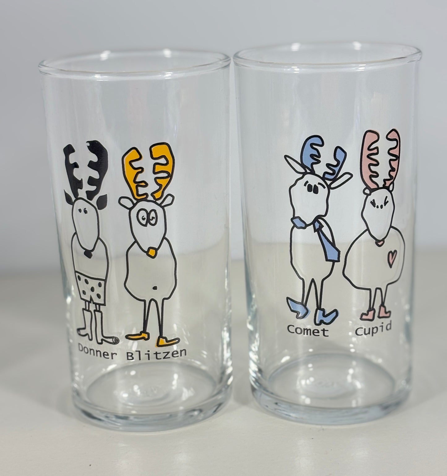 Two clear glasses with cartoon reindeer designs on a gray background