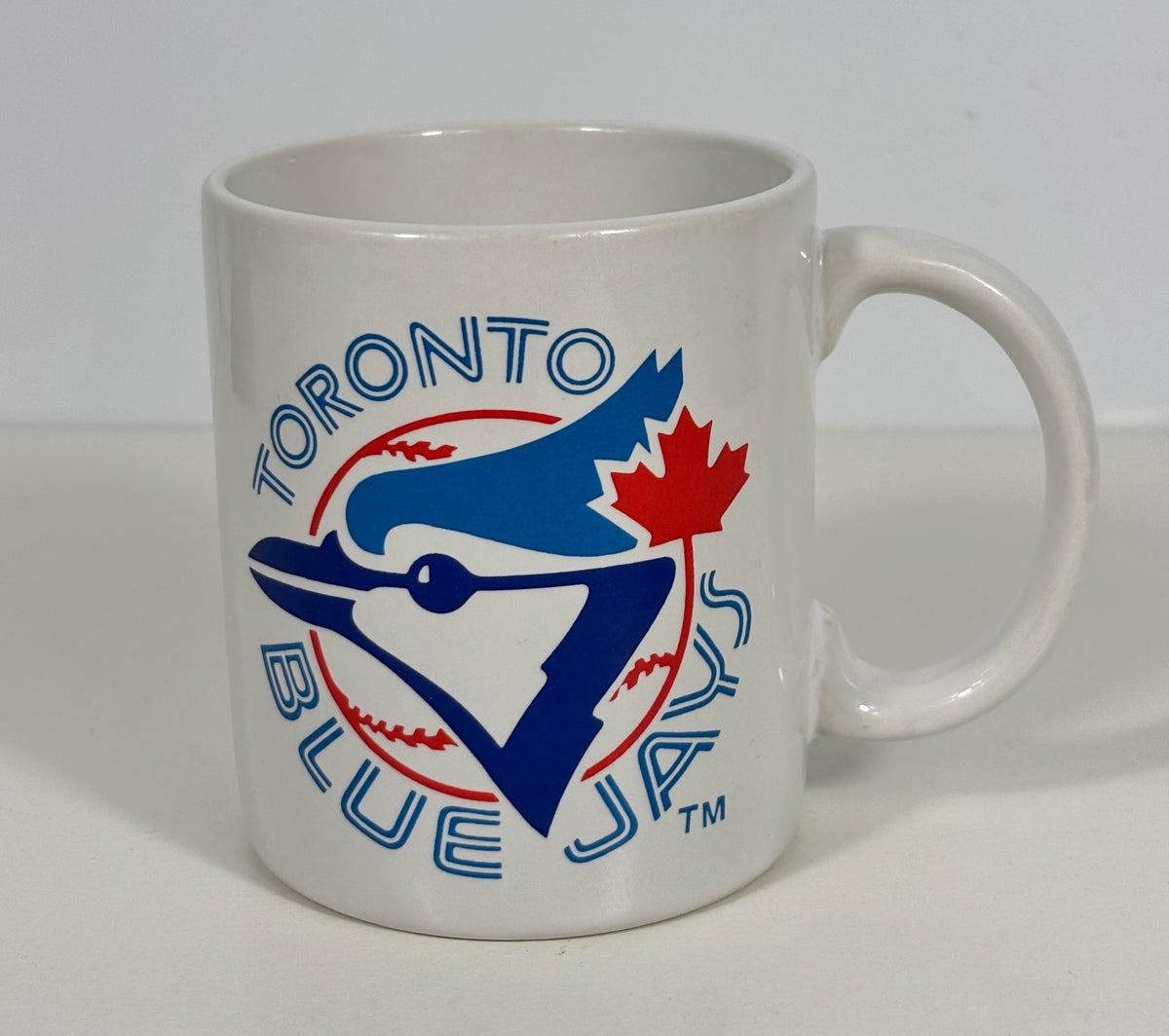 A white ceramic Toronto Blue Jays coffee mug featuring the team logo in blue, red, and white, set against a plain light gray background.