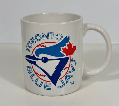 A white ceramic Toronto Blue Jays coffee mug featuring the team logo in blue, red, and white, set against a plain light gray background.