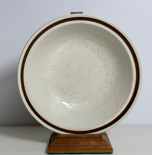 Speckled ceramic bowl with brown rim on a wooden stand against a white background