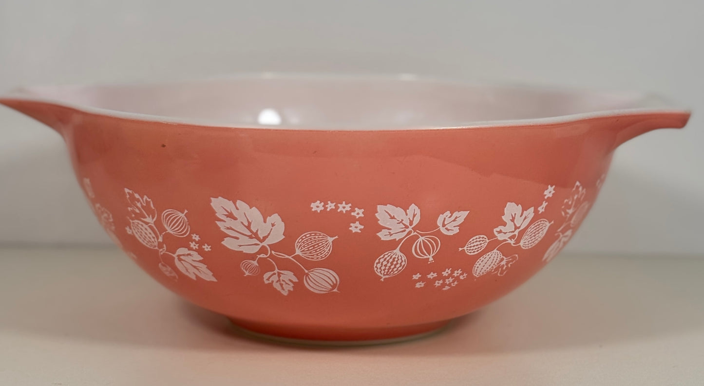 A vintage pink Pyrex mixing bowl with a white berry and floral pattern, featuring side handles and a glossy finish.