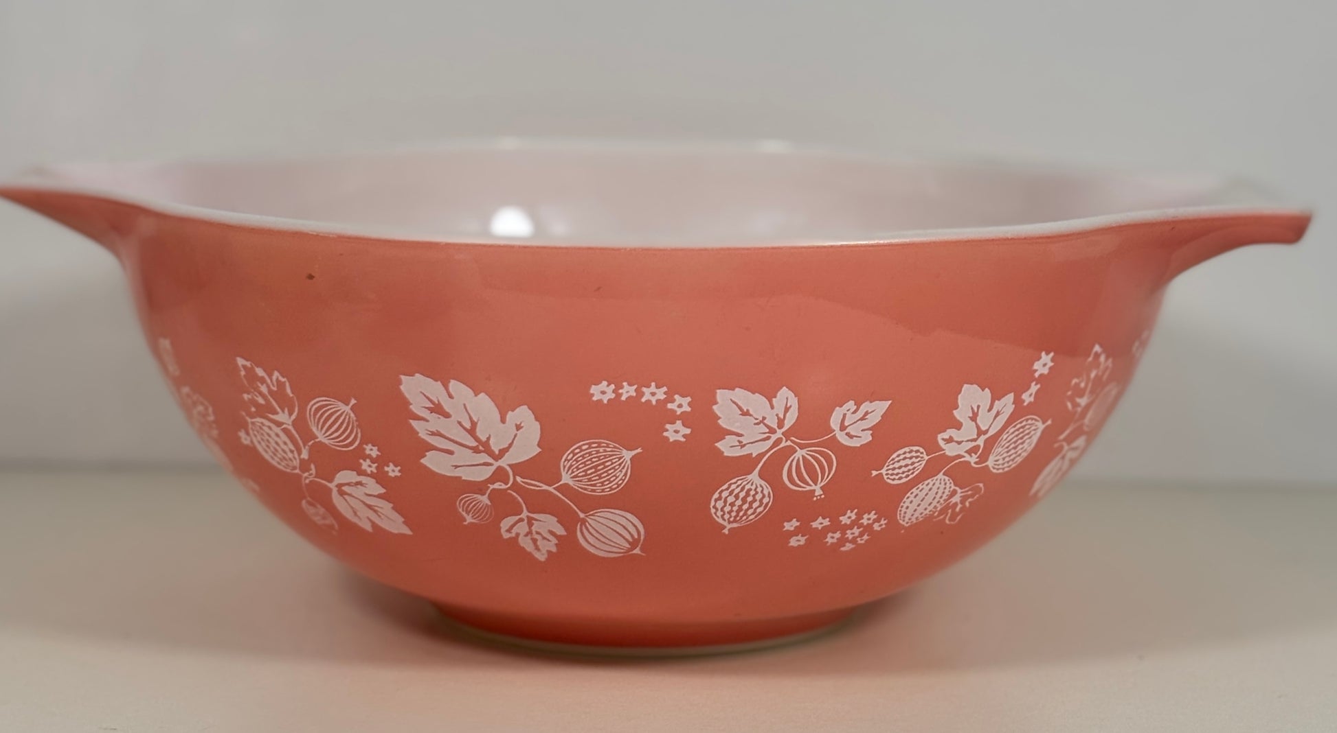 A vintage pink Pyrex mixing bowl with a white berry and floral pattern, featuring side handles and a glossy finish.