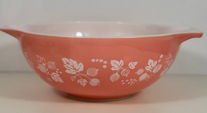A vintage pink Pyrex mixing bowl with a white berry and floral pattern, featuring side handles and a glossy finish.