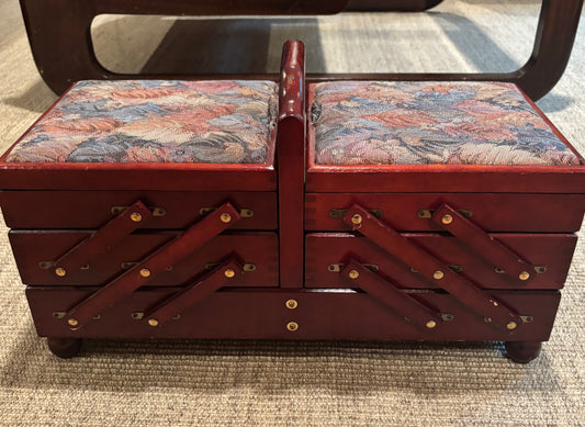 A vintage wooden storage chest with two compartments, featuring patterned fabric-covered top lids and dark reddish-brown wood drawers with decorative metal brackets.