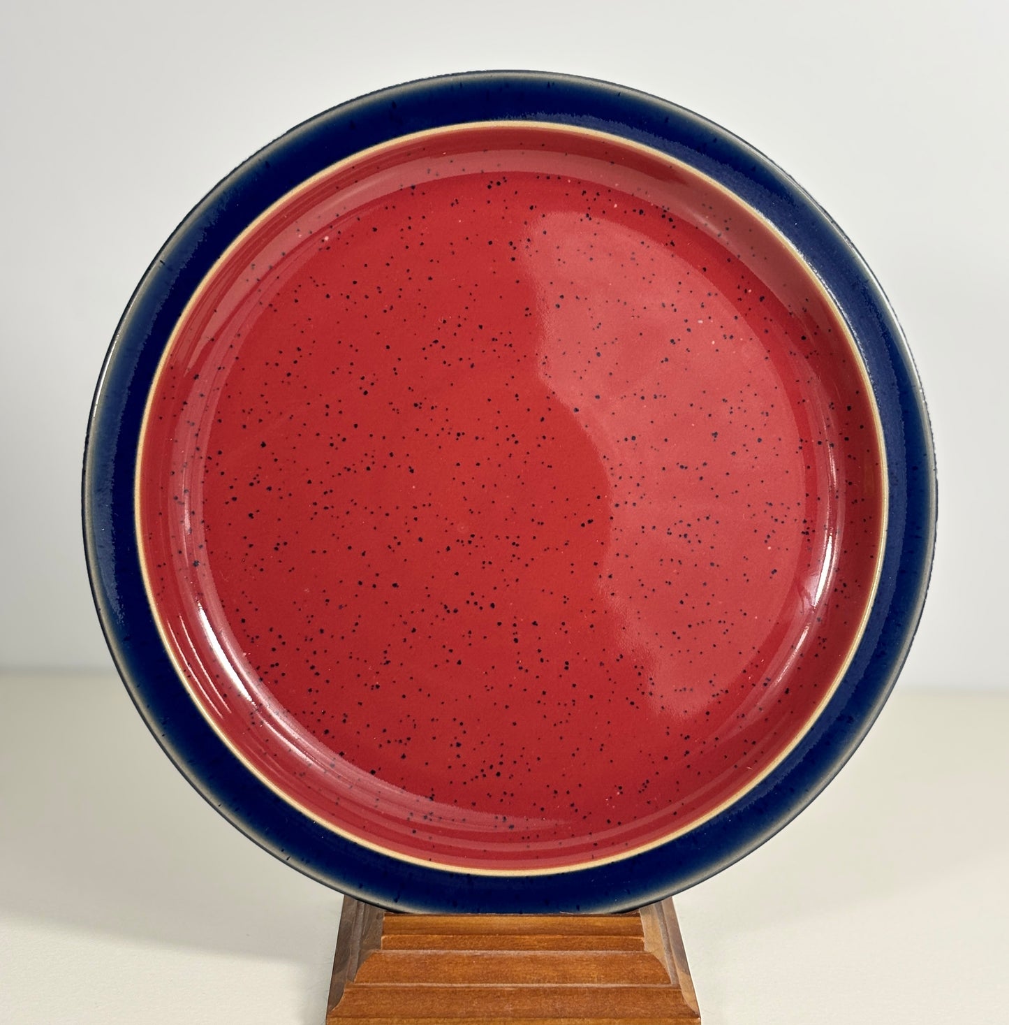 Ceramic plate with red glaze and blue rim on a stand against a white background