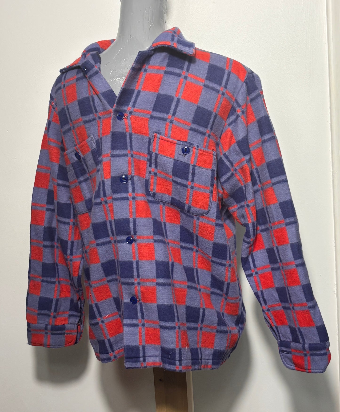A long-sleeve plaid button-up shirt displayed on a mannequin torso. The shirt features a checkered pattern of red, navy blue, and gray, with matching dark buttons and a chest pocket.