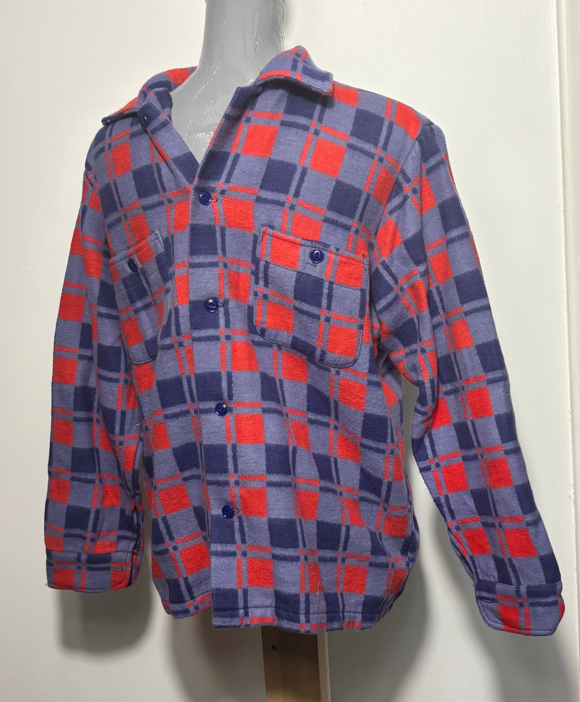 A long-sleeve plaid button-up shirt displayed on a mannequin torso. The shirt features a checkered pattern of red, navy blue, and gray, with matching dark buttons and a chest pocket.