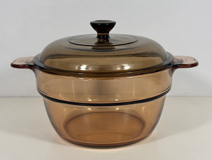 A vintage amber-brown glass casserole dish with a matching glass lid and side handles, photographed against a plain white background.