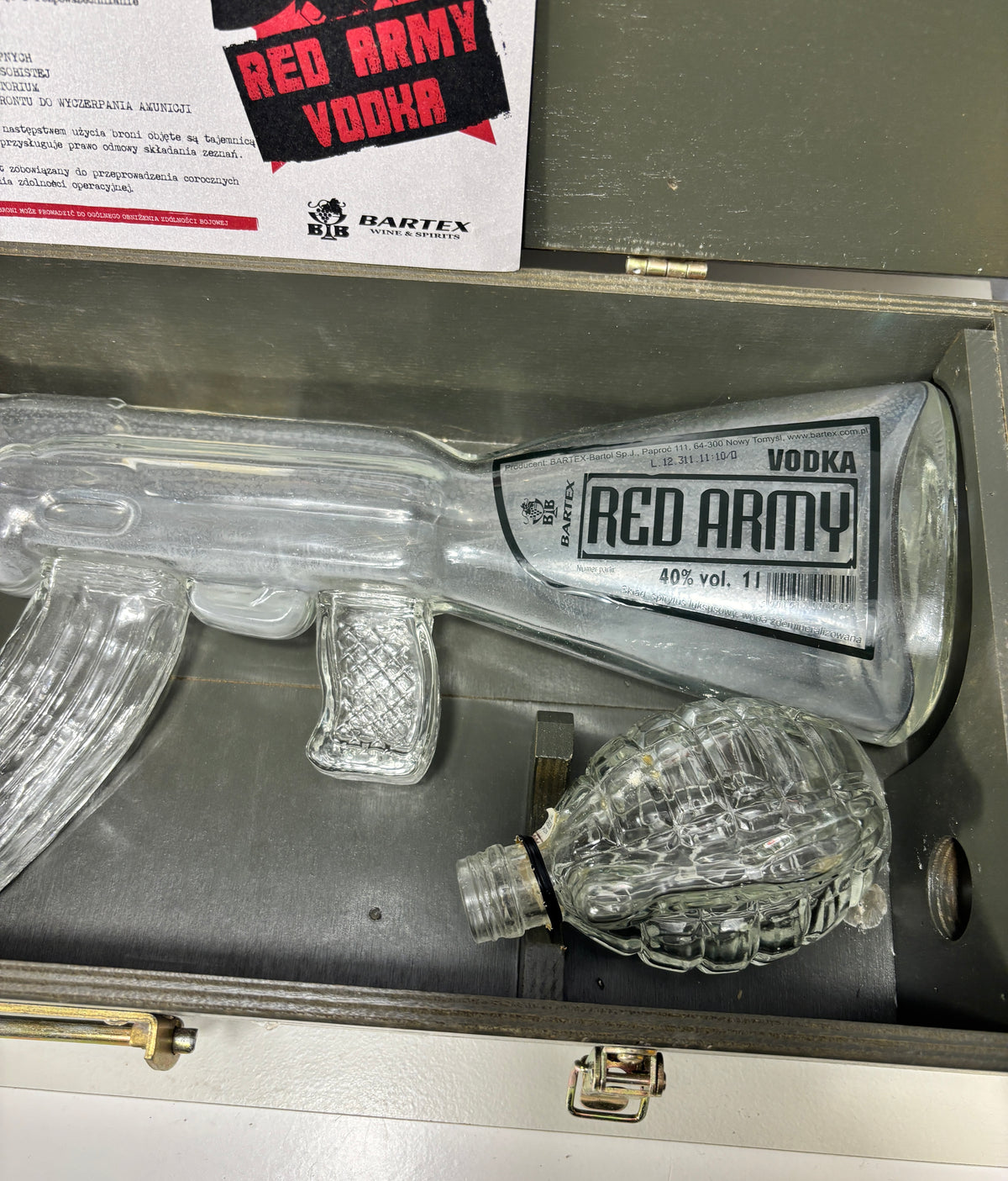 A clear plastic replica of a Bartex Red Army Vodka bottle and matching glass decanter displayed inside a gray metal case, with a branded paper insert visible at the top.
