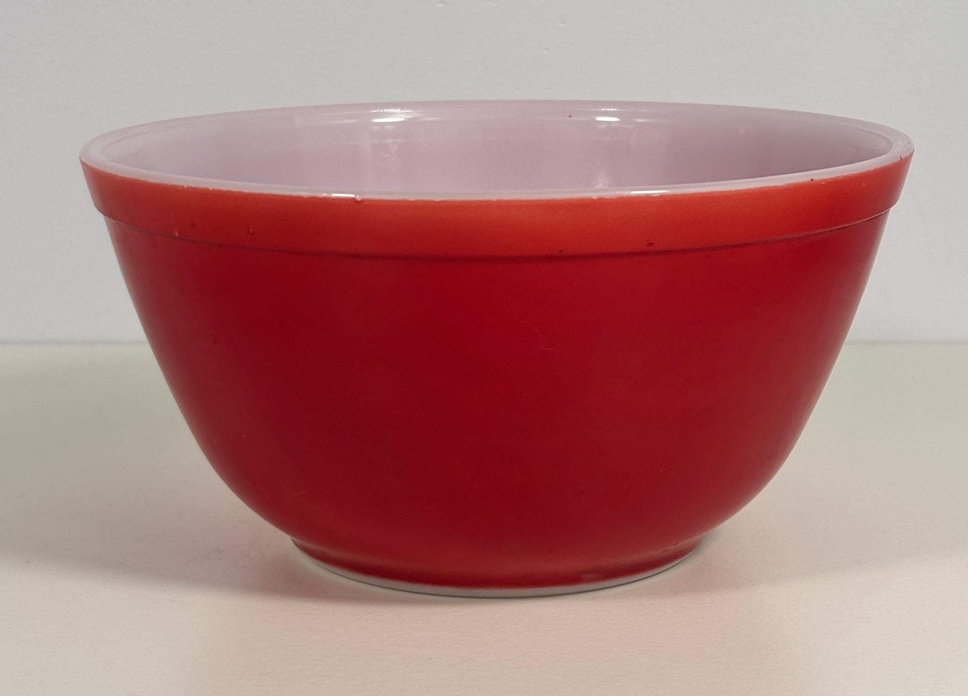 A red glass mixing bowl with a red exterior, photographed against a plain light background.
