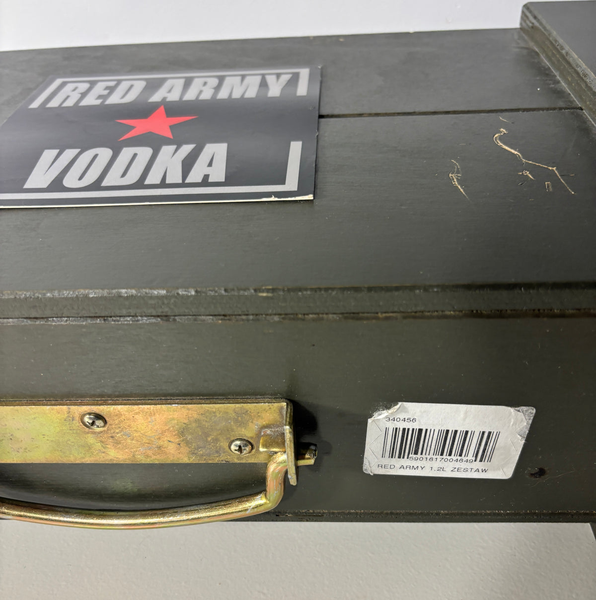 A vintage military-style wooden box in dark olive green with a metal handle, featuring a 'RED ARMY VODKA' sticker on top and a barcode label near the handle.