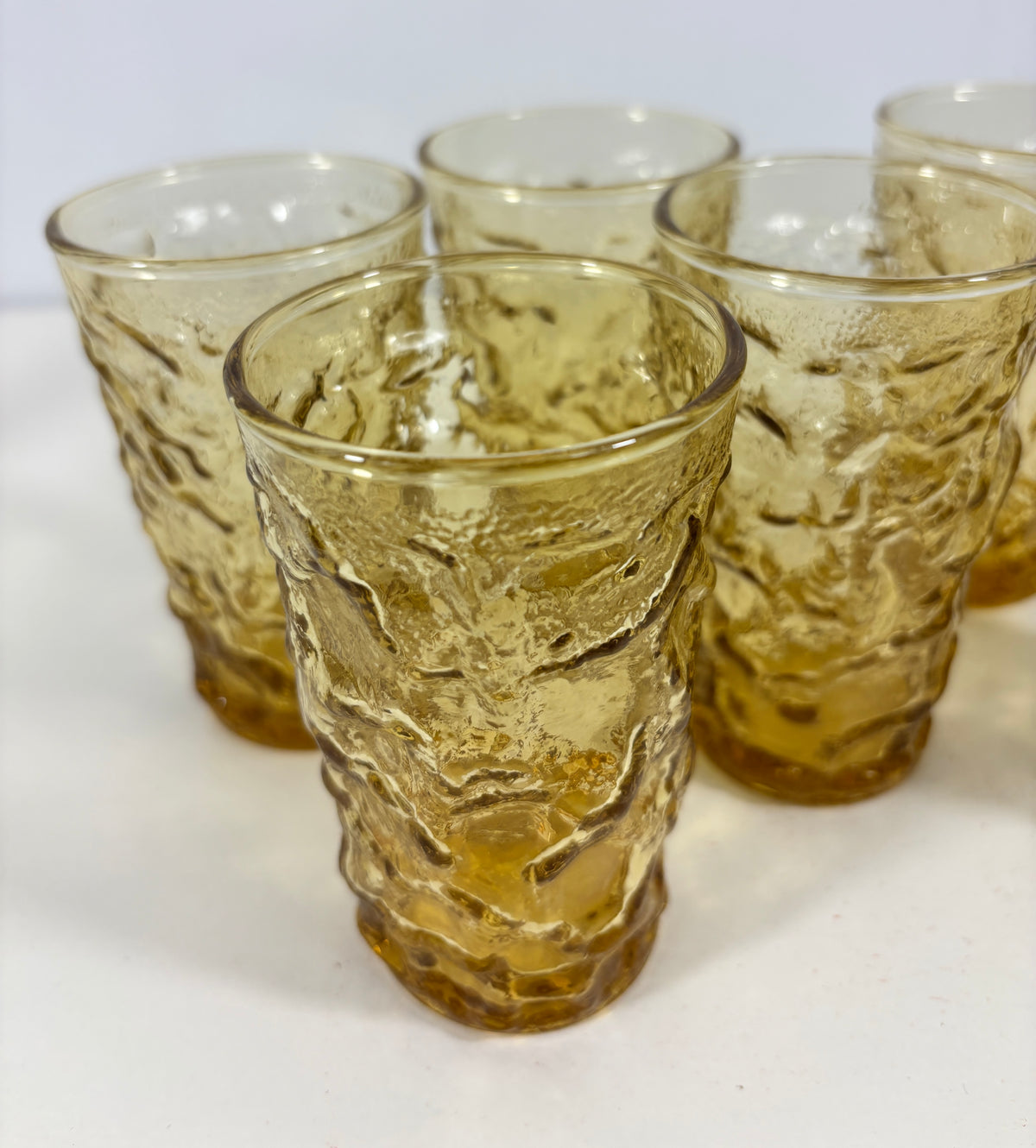 A set of five textured amber glass tumblers arranged on a white surface against a light gray background.