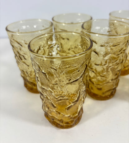 A set of five textured amber glass tumblers arranged on a white surface against a light gray background.