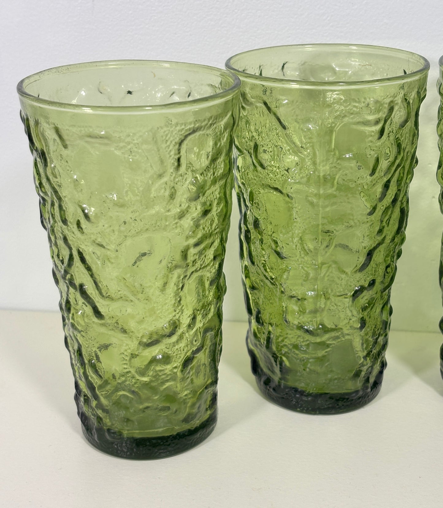Two green textured glass tumblers on a white surface with a white background