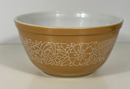 A vintage Pyrex mixing bowl in a warm tan-brown color with a white floral line-art pattern on the outside and a white glazed interior.