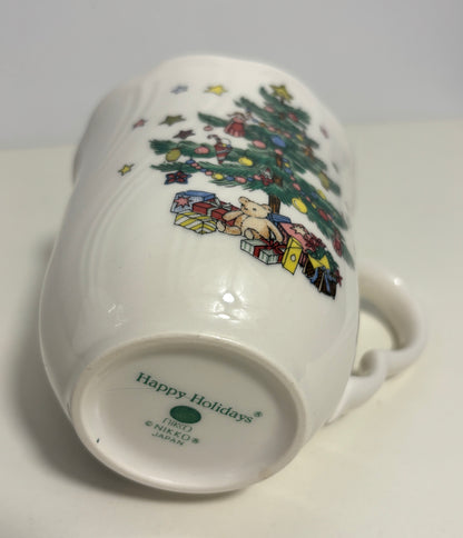 A white ceramic mug shown from its bottom side, featuring a colorful illustration of a decorated Christmas tree and wrapped gifts. The inside bottom is printed with 'Happy Holidays' and 'Nikko Japan'.