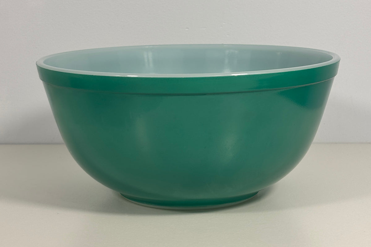 A classic round mixing bowl with a glossy teal green exterior and a light blue interior, photographed against a neutral off-white background.