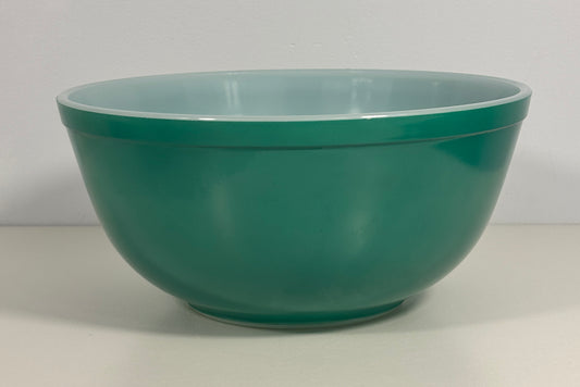 A classic round mixing bowl with a glossy teal green exterior and a light blue interior, photographed against a neutral off-white background.