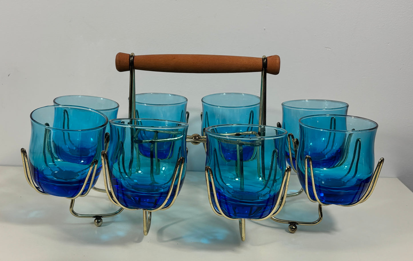 A vintage six-piece blue glass ice bucket set with a wooden handle and brass-colored metal stand, displayed on a white surface against a white background.