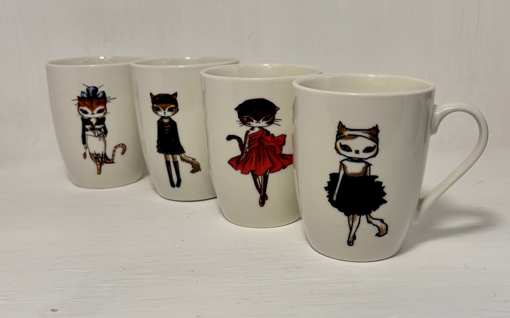 Set of four mugs with illustrated cat characters on a white background