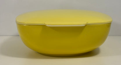 A bright yellow oval lidded container or dish with a matching yellow lid, photographed against a plain light background.