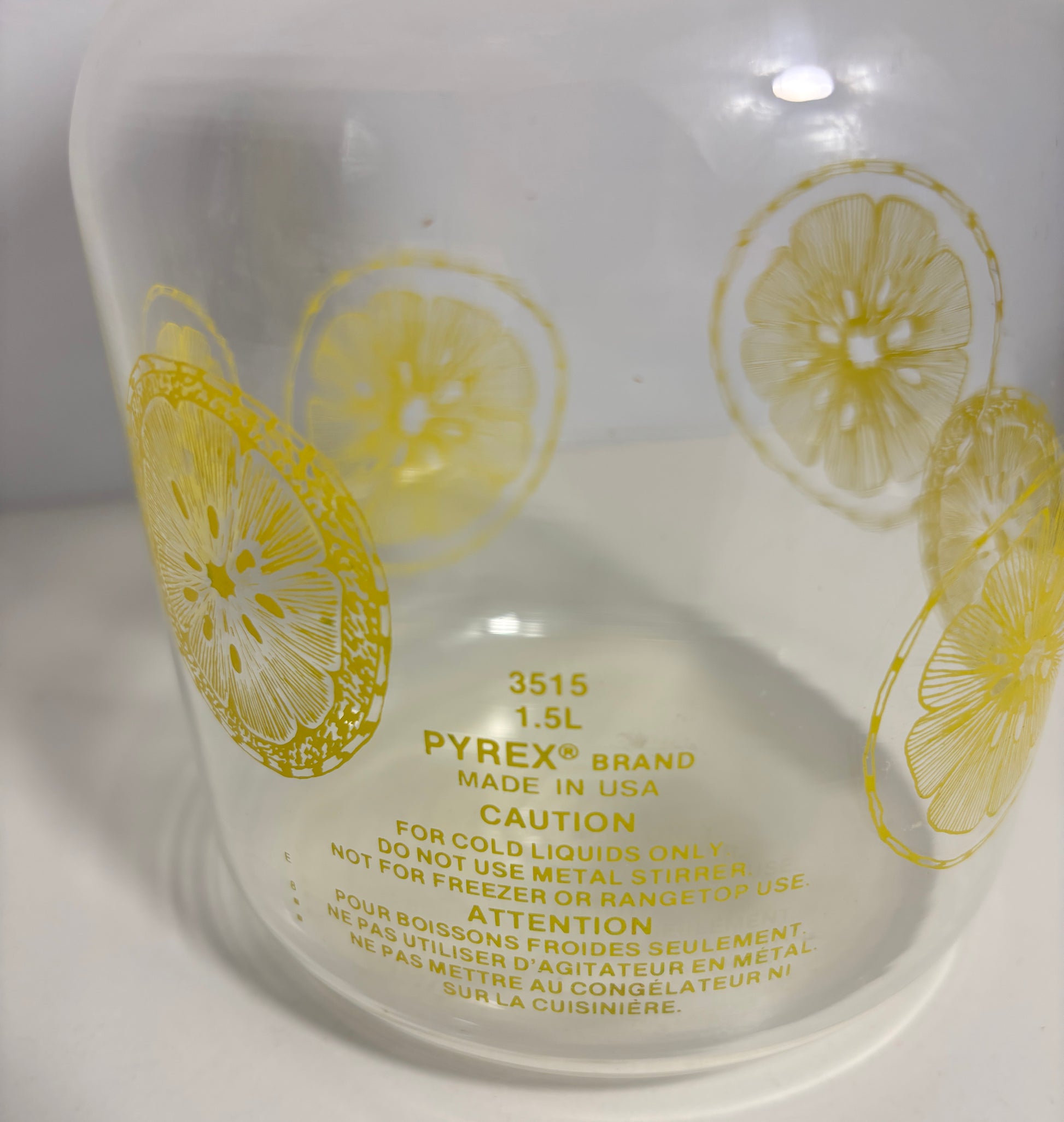 A close-up of a clear Pyrex glass container with yellow printed lemon slice patterns and safety text on a white background.