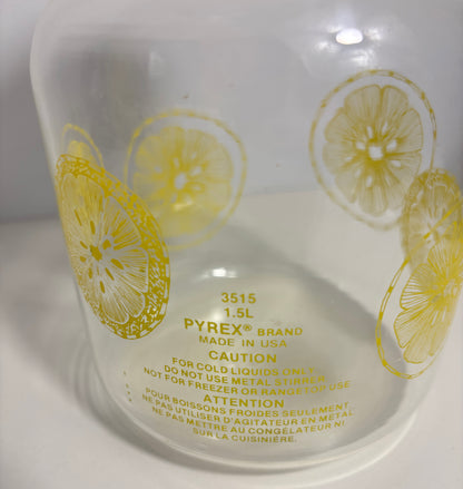 A close-up of a clear Pyrex glass container with yellow printed lemon slice patterns and safety text on a white background.