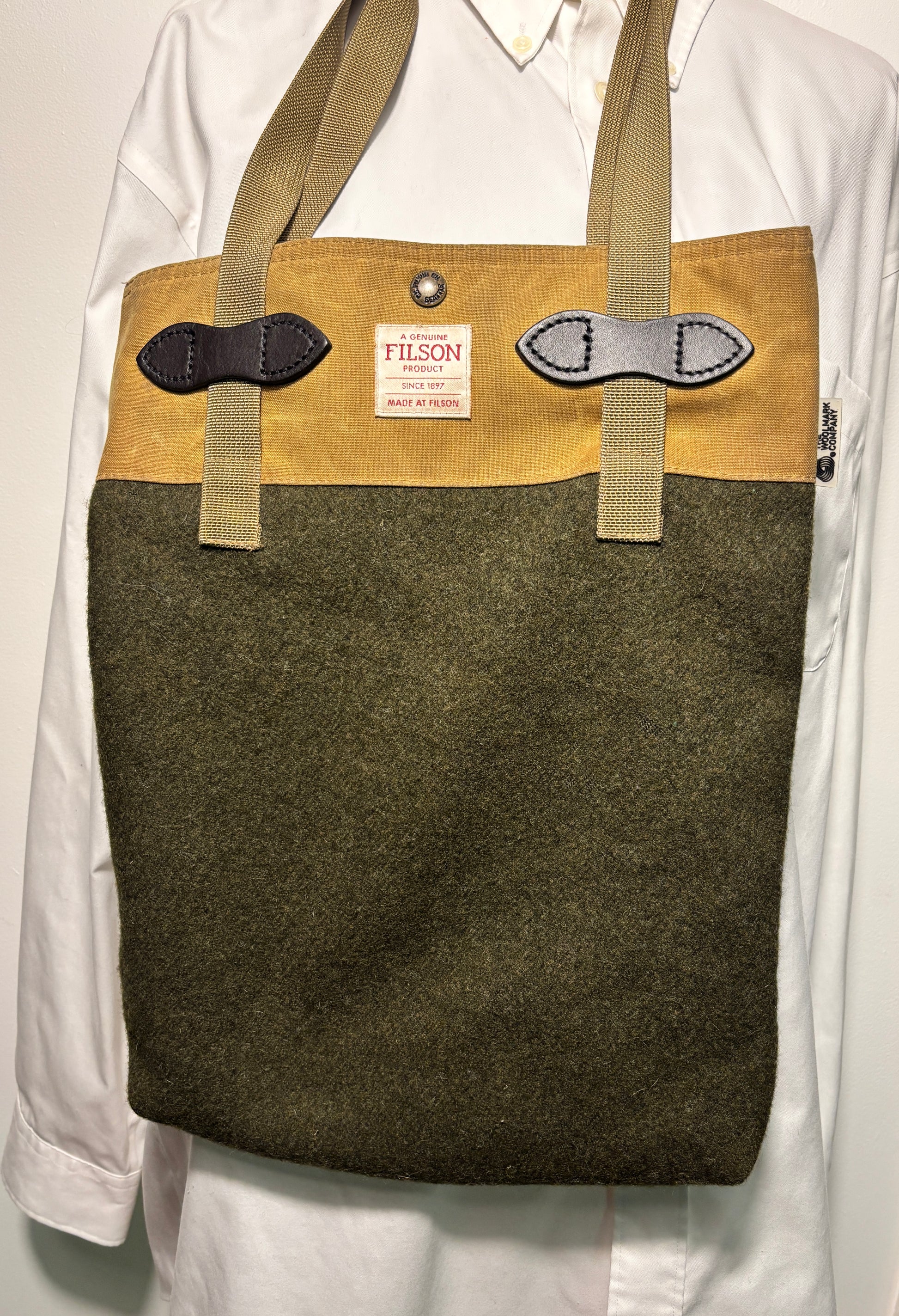 Brown tote bag with green front section and visible Filson label on a white background