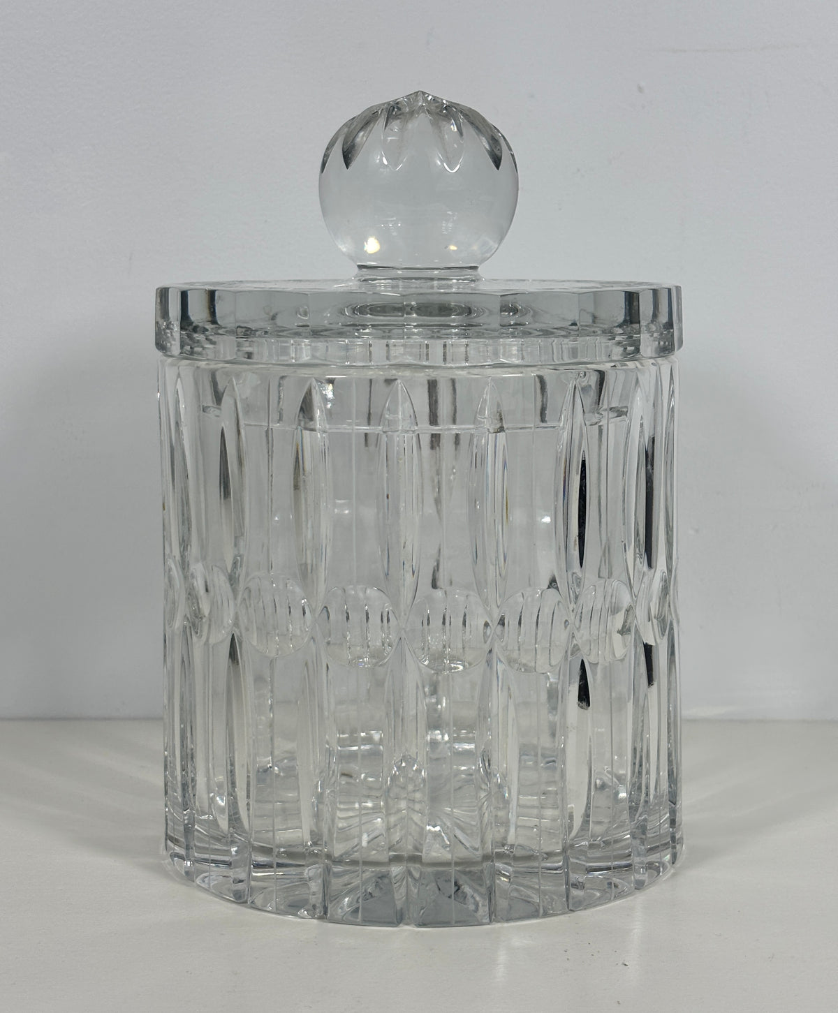 A clear cut-glass or crystal cylindrical container with a matching round glass lid, photographed against a plain light background.