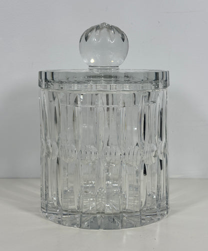 A clear cut-glass or crystal cylindrical container with a matching round glass lid, photographed against a plain light background.
