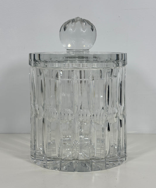 A clear cut-glass or crystal cylindrical container with a matching round glass lid, photographed against a plain light background.