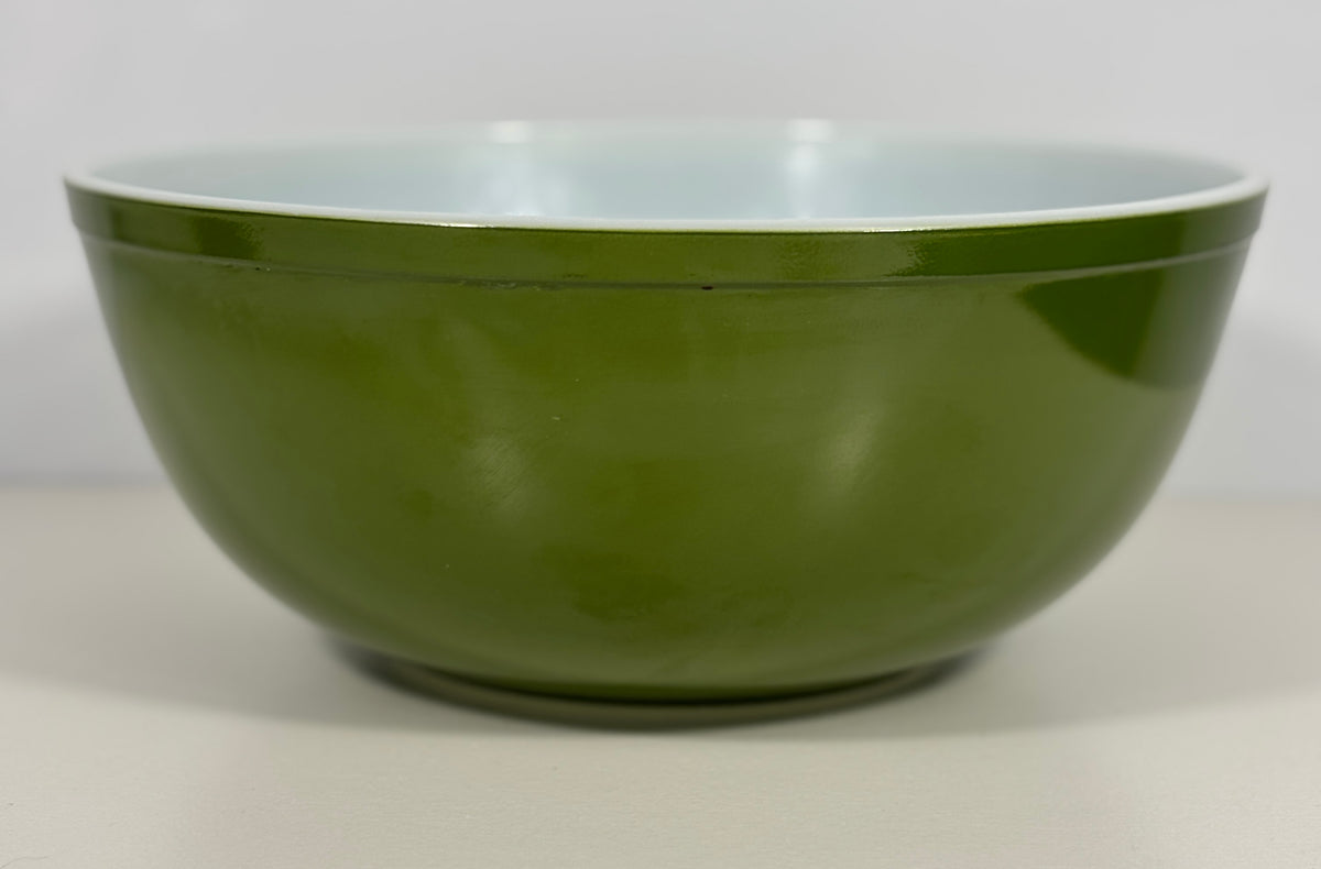 A green mixing bowl with a glossy finish and a contrasting light blue interior, shown against a neutral light gray background.