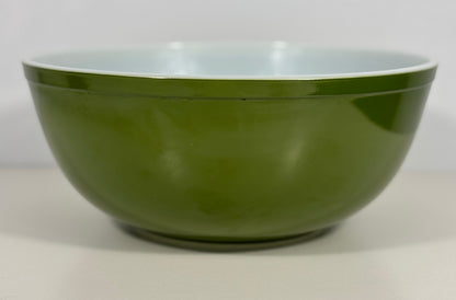 A green mixing bowl with a glossy finish and a contrasting light blue interior, shown against a neutral light gray background.