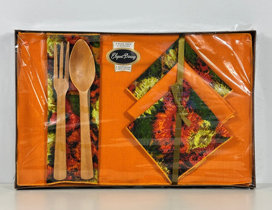 A boxed tableware set in clear plastic wrapping, featuring orange napkins with a floral autumn pattern and light wood-colored utensils on a white background.