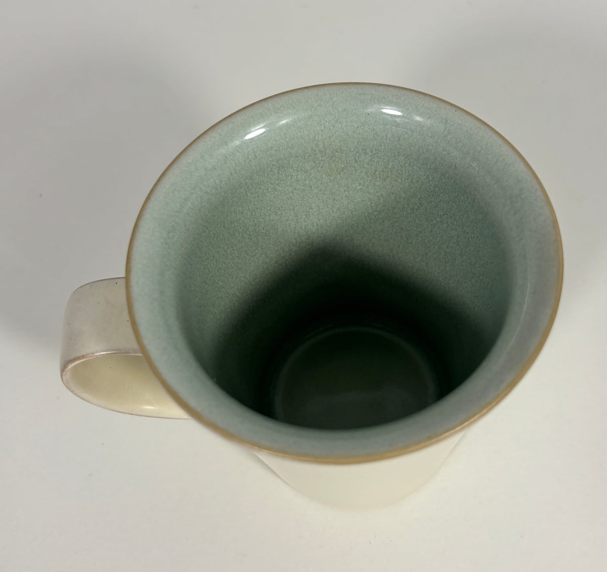 An off-white ceramic mug with a speckled sage green glazed interior and a thin gold rim, shown from a top-down perspective on a light gray background.
