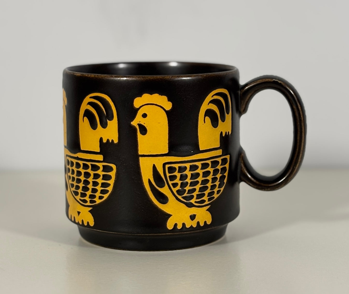 brown mug with yellow rooster designs on a light gray background