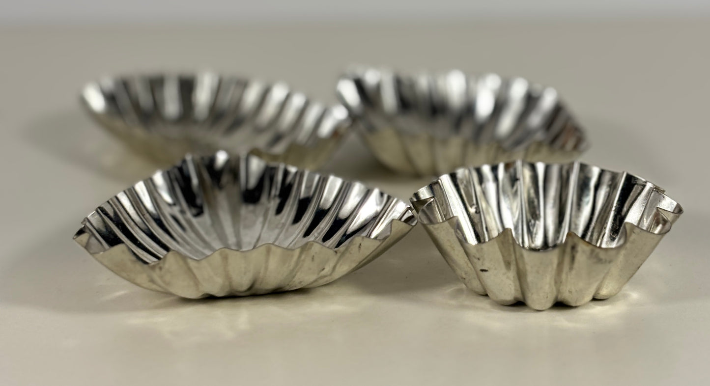 Four silver fluted tart tins on a light background