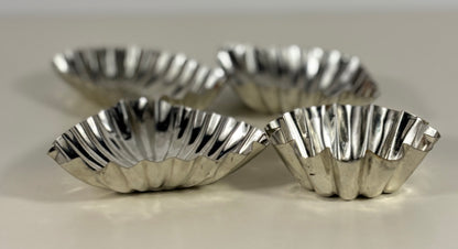 Four silver fluted tart tins on a light background