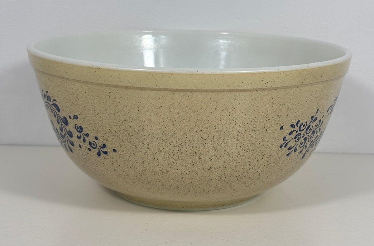 A large speckled beige ceramic mixing bowl with a white interior and blue floral scroll patterns on the sides, set against a plain white background.