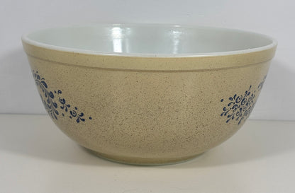 A large speckled beige ceramic mixing bowl with a white interior and blue floral scroll patterns on the sides, set against a plain white background.