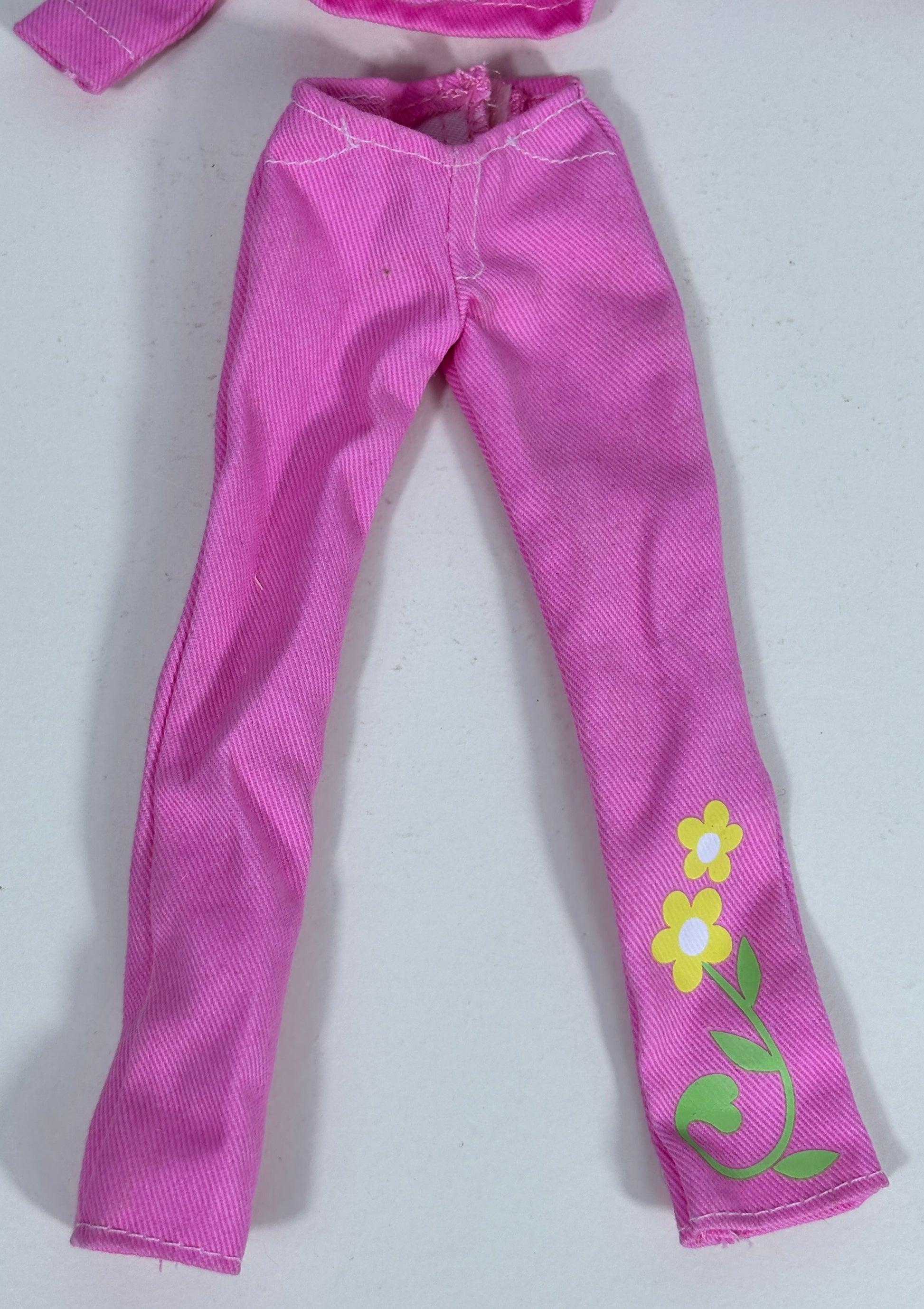 Pink doll pants with a textured fabric, featuring a yellow and white flower and green vine print on one leg, shown on a light gray background.