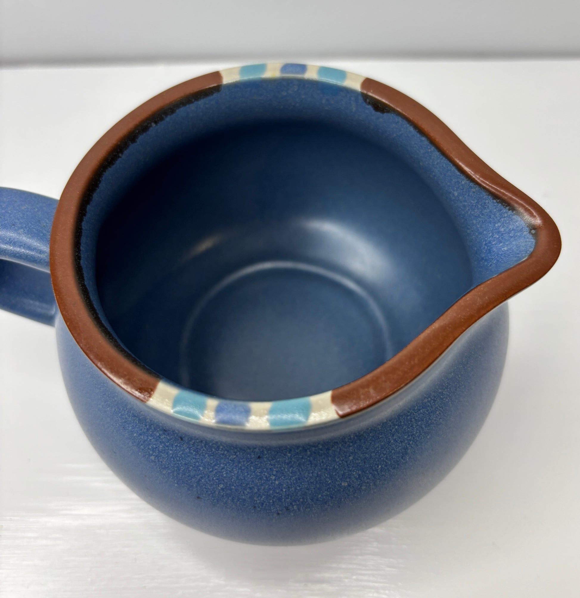 Blue ceramic pitcher with brown handle on a white background