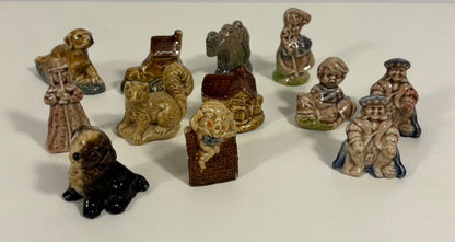 A group of small ceramic figurines and animal-shaped objects arranged on a plain light background. The set includes figures in clothing, a dog, a cat, a bird, a house, and other decorative shapes, mostly in earthy beige, brown, gray, and black tones.