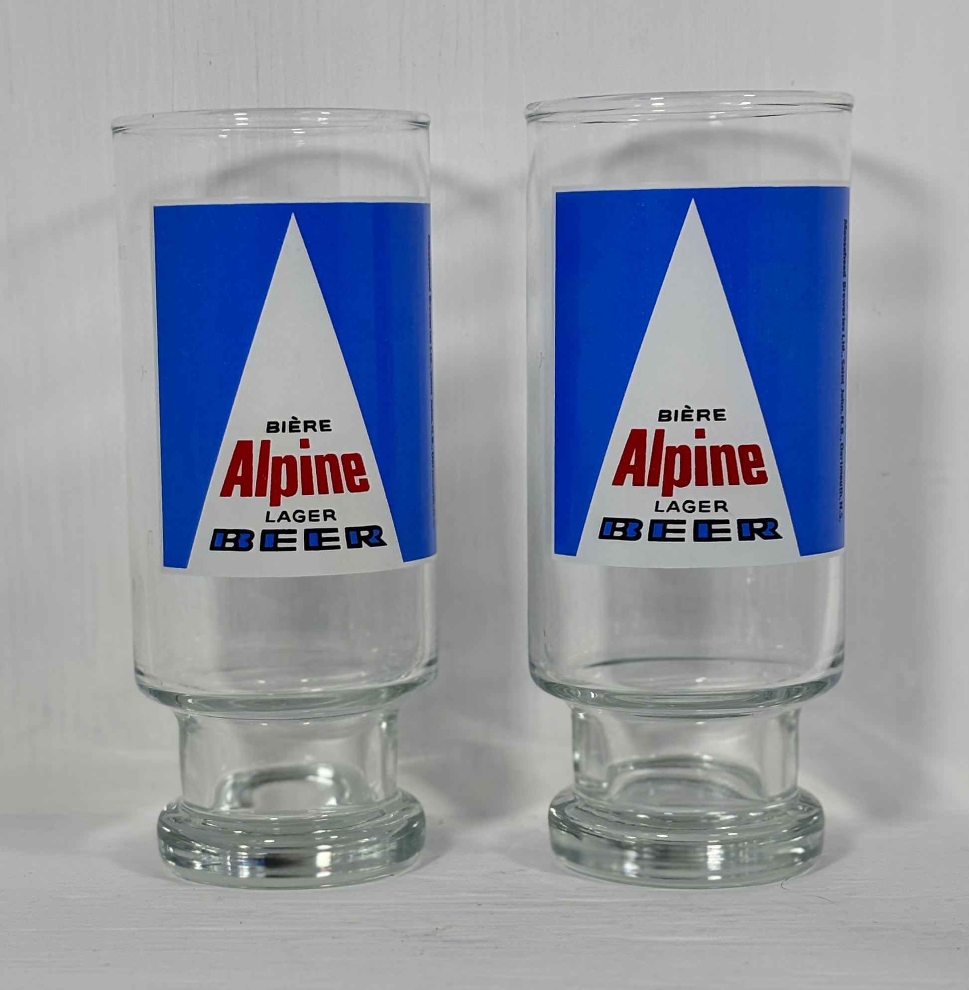 Two glass tumblers with Alpine Lager Beer label on a white background