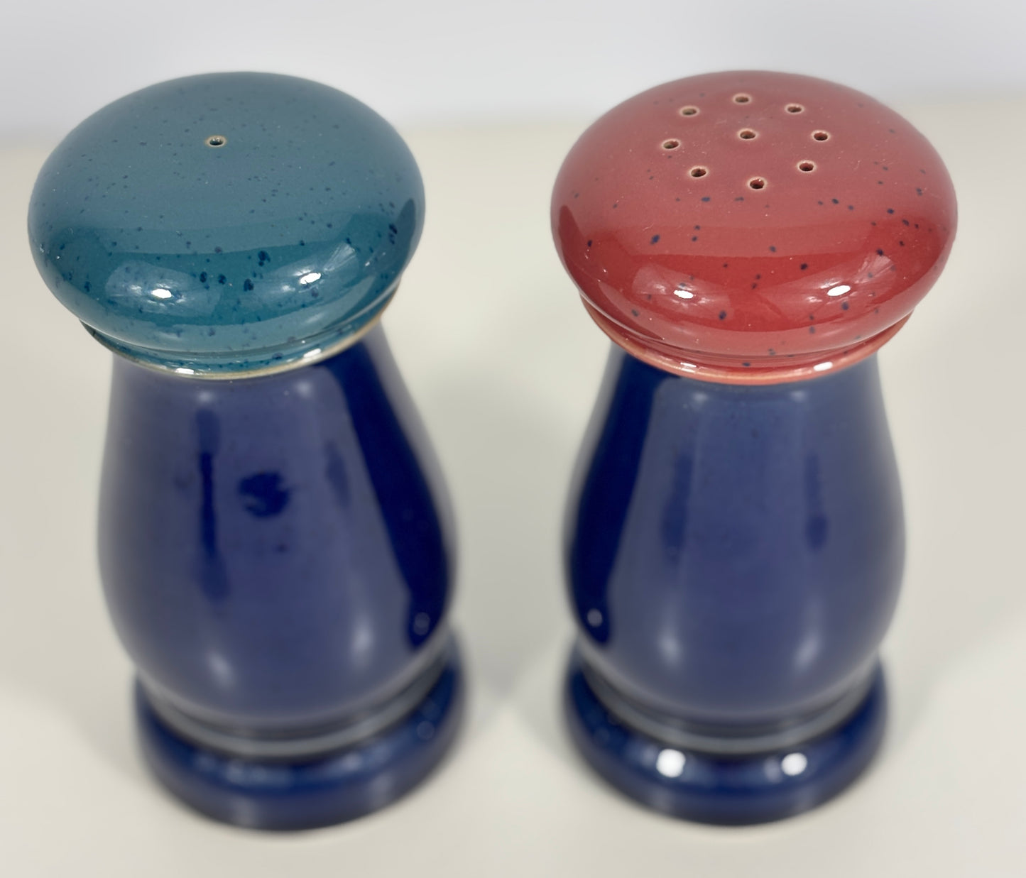 Two ceramic salt and pepper shakers with blue and red speckled tops on a white background