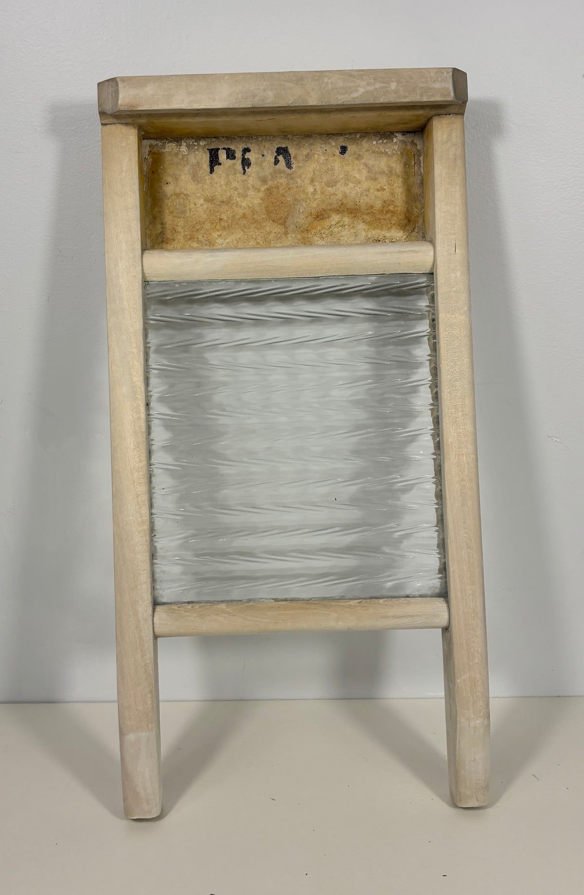 A vintage wooden washboard with a clear glass or plastic central panel and a light natural wood frame, photographed against a plain off-white background.