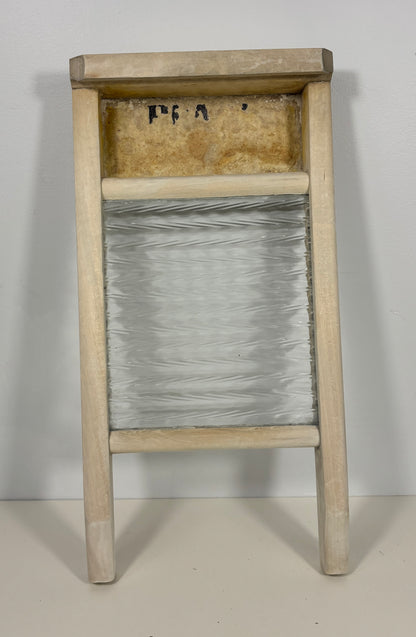 A vintage wooden washboard with a clear glass or plastic central panel and a light natural wood frame, photographed against a plain off-white background.