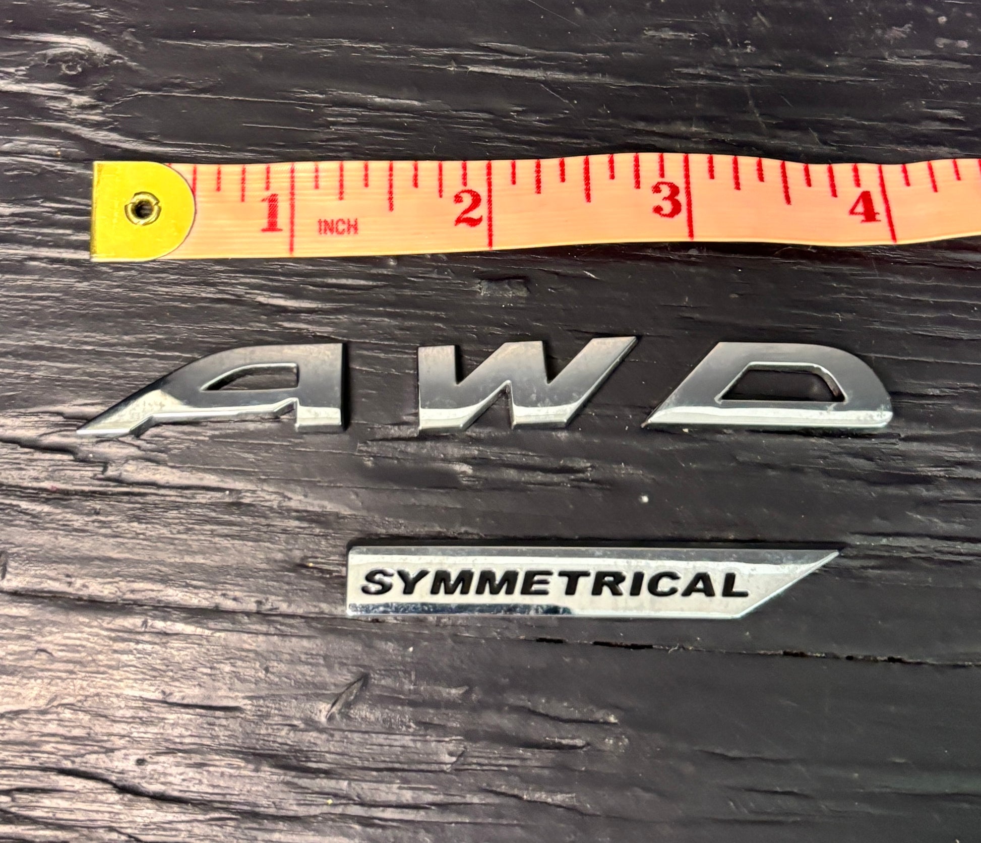 AWD emblem with a ruler for scale on a wooden surface