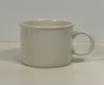 A plain white ceramic mug with a simple cylindrical shape and a loop handle, shown against a neutral off-white background.